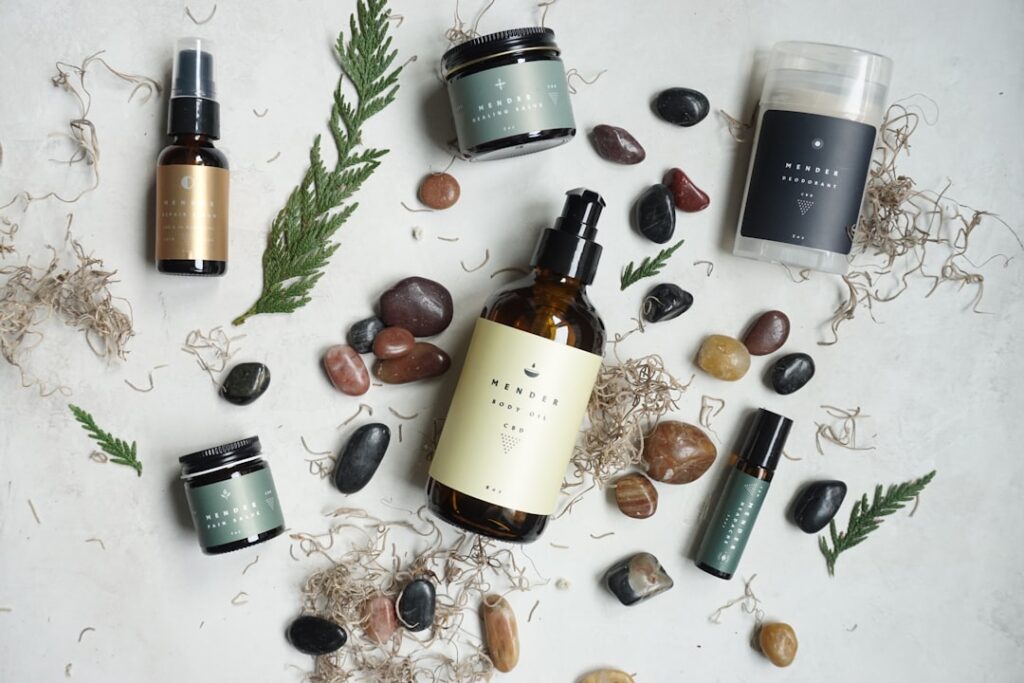 Produtos de beleza sobre mesa de vidro com luz natural e plantas ao fundo.